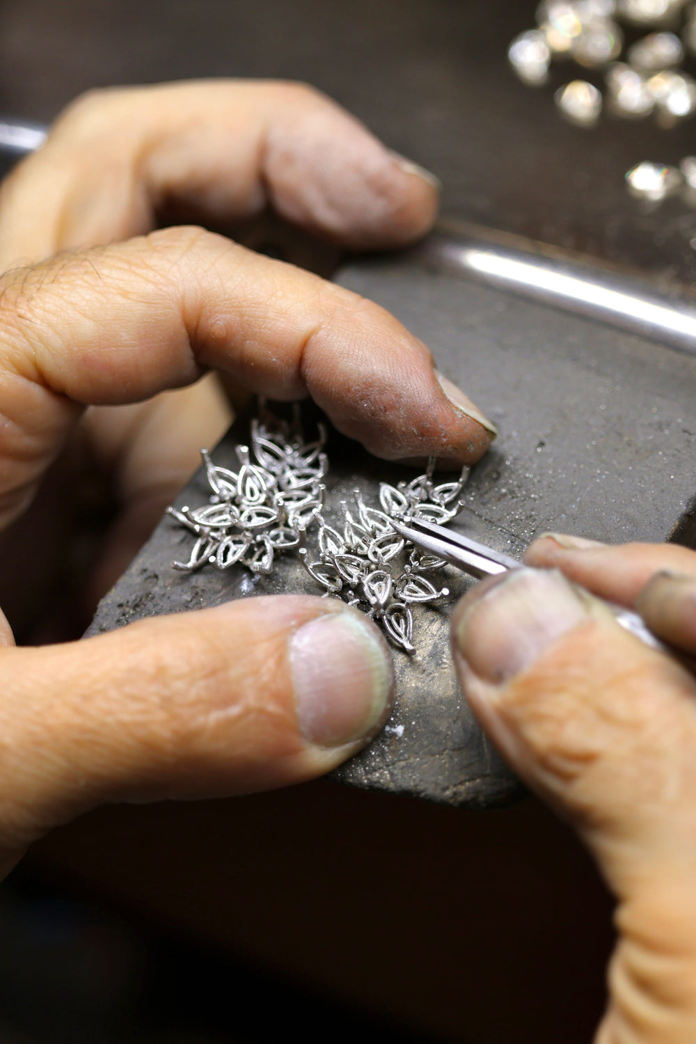 Close-up of hands working on white gold jewelry with a focus on craftsmanship.