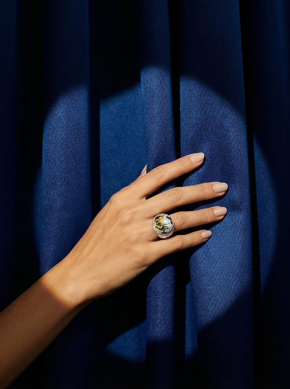 Hand wearing a ring with a colorful stone against a blue fabric background