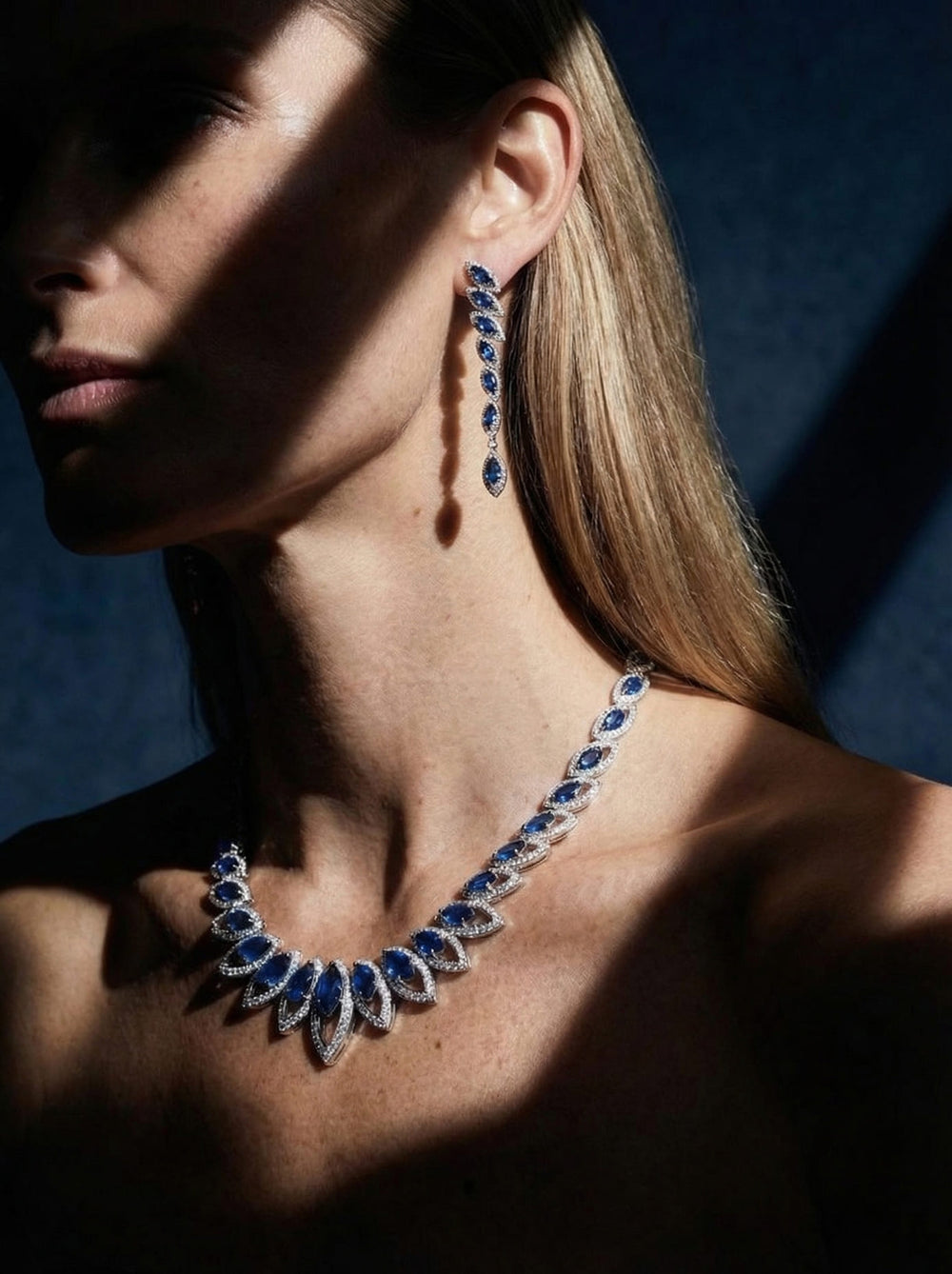 Close-up of a woman wearing a blue and silver necklace and earrings against a dark background